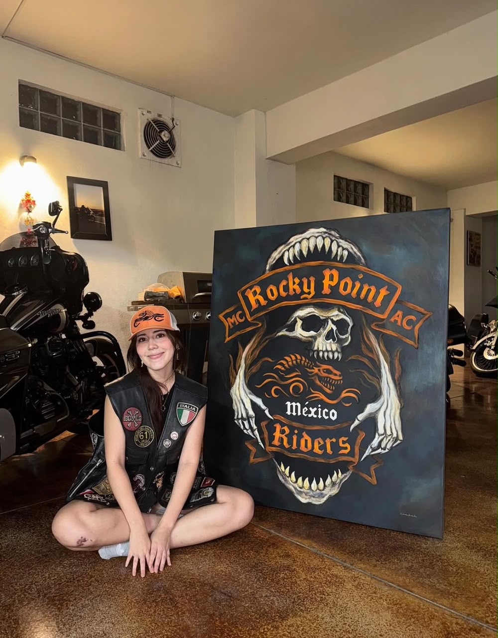 Artist Isabel sitting with a large custom Rocky Point Riders commission painting in her studio